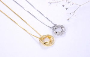 Detail von ineinandergreifenden Dreiring-Anhängern in Gold und Silber mit Zirkonia-Besatz