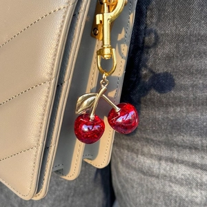 Shiny red cherry charm keychain with gold lobster clasp on a quilted grey leather bag