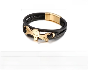 Detail view of a black braided leather bracelet featuring a gold skull and wrench motif
