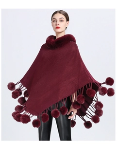 Detail of burgundy knit poncho featuring a faux rabbit fur collar and fluffy pom-pom tassels