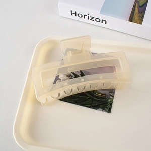 Detail of a large matte cream-yellow rectangular hair claw clip on a stylish tray