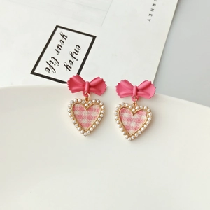 Detailed close-up of bow earrings featuring pink checkered hearts and pearl beads