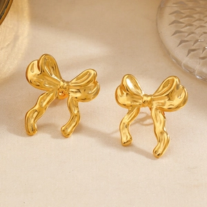 Elegant gold bow-shaped metal stud earrings displayed on textured beige fabric background