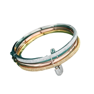 Three-tone stackable crystal bangles in gold, silver, and rose gold with safety pin charms