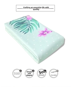 Detail view of microfiber beach towel featuring tropical green leaves and floral patterns