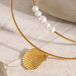 Detail of 18k gold stainless steel bangle with shell pendant and fine pearl wire bracelet