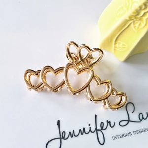 Detail of golden heart-shaped metal hair claw clip with hollow design and glossy finish