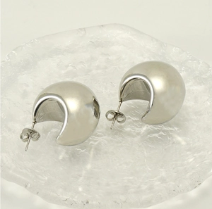 Close-up of C-shaped silver earrings with a brushed metal finish on a glass tray