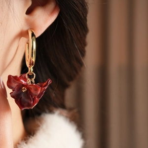 Close-up of model wearing burgundy petal flower earrings with golden C-shape metal hoop