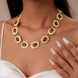 Close-up of retro gold sweater necklace with dark red gems and tiny white flowers