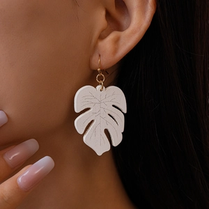Close-up of white monstera leaf earring with golden hook worn by a female model