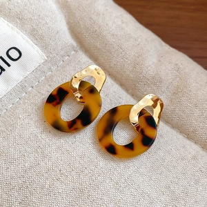 Macro shot of geometric leopard print acetate earrings with gold metal rings on linen cloth