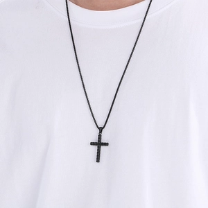 Détail d'un pendentif croix noire texturée sur une chaîne vénitienne portée sur un t-shirt