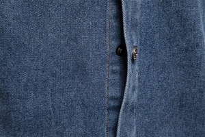 Detailed close-up of dark blue denim shirt with durable orange stitching and metal button