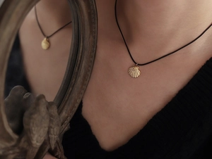 Detail of a golden shell pendant on a black cord necklace, shown in a mirror reflection