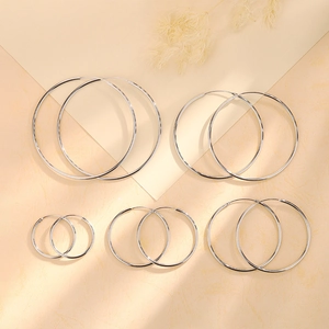 Detailed comparison of five sizes of polished silver hoop earrings on warm beige background