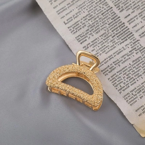 Close-up of golden metal D-shaped hair claw clip with textured finish on vintage book page