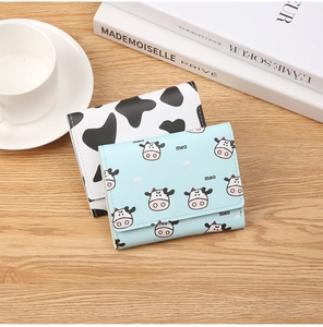 Close-up of cow print and blue cartoon mini wallets on a wooden surface with lifestyle decor