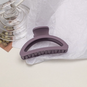 Detail view of a matte purple semi-circular shark hair claw clip on white crinkle paper