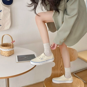 Gros plan de baskets en toile blanc crème avec rayures bleues portées par un mannequin
