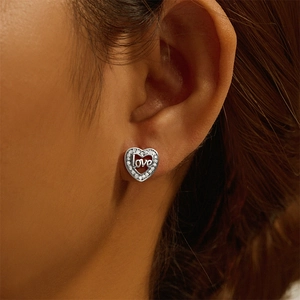 Detailed macro view of heart-shaped silver stud earrings with love script and zircons