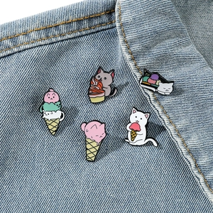 Five cute cartoon cat enamel pins shaped like ice cream cones on a denim jacket collar