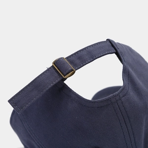 Detail of dark blue canvas baseball cap featuring an adjustable brass metal buckle closure