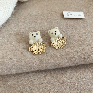 Detailed macro view of 18K gold-plated flocked bear earrings on soft wool background