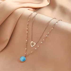 Rose gold double-layer necklace with heart and blue round stone pendants on silk background