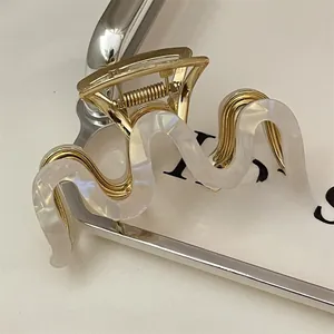 Detailed side view of wave-shaped gold metal hair claw with white acetate pearl finish