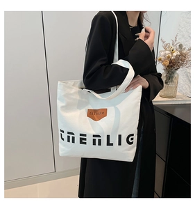 Detail of a large white canvas tote bag with black lettering and leather trim on a model