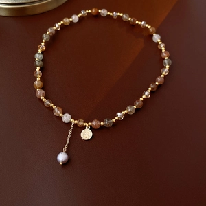 Detail of multi-layered beaded bracelet with brown stones and a golden pearl pendant