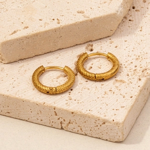 Detail of 18K gold-plated hoop earrings with intricate woven texture on stone surface