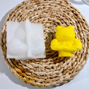 Detailed silicone mold showing muscle bear shape and finished yellow candle on straw mat