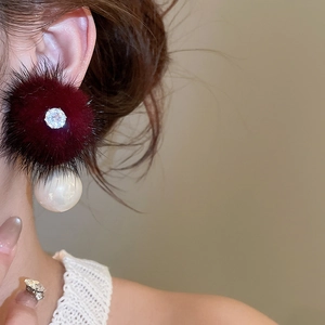 Detail of burgundy fur pompom earring with zircon inlay and large white pearl accent