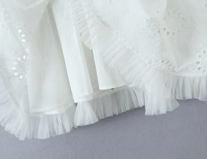 Détail de la broderie ajourée blanche et de l'ourlet en tulle plissé sur la robe