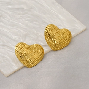 Macro shot of gold heart earrings featuring unique basket weave texture on marble surface