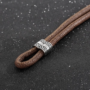 Macro shot of brown braided leather cord with engraved geometric silver steel clasp