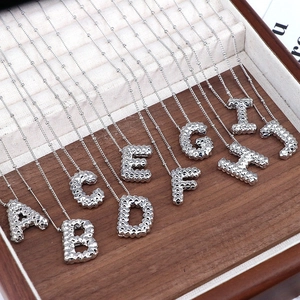 Detail view of silver embossed alphabet pendants from A to J on a white jewelry lining
