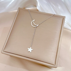 Polished silver crescent moon and star Y-necklace on a champagne jewelry box surface