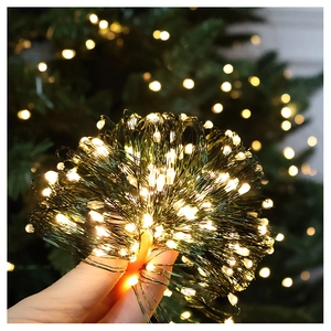 Close-up of warm white LED firefly lights on green copper wire with holiday bokeh background