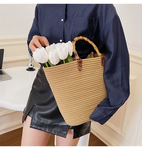 Detail of woven straw tote bag with bamboo handle and brown leather rivet accents