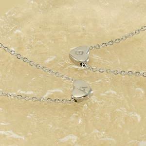 Minimalist silver heart letter necklaces with A and B engravings on textured background
