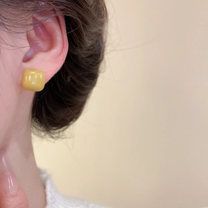 Close-up of square yellow resin stud earring with glossy finish on model ear