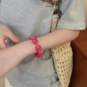 Macro shot of irregular magenta resin beads bracelet with golden spacers worn by model