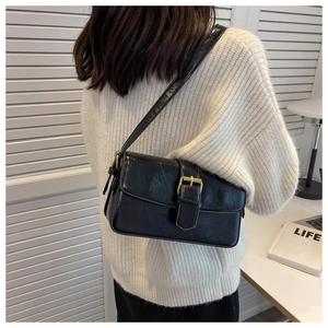 Close-up of black oily leather shoulder bag with gold buckle on a knitted sweater