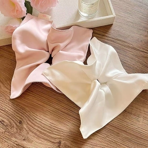 Close-up of pink and white large satin scrunchies with bow design on a wooden surface