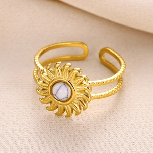 Macro shot of sun-shaped gold titanium ring with white natural stone on beige fabric