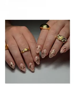 Detailed view of 3D gold bowknot nail charms and textured metallic rings on fingers
