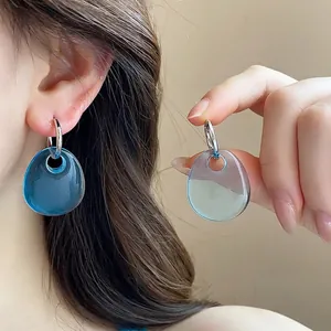 Close-up of blue teardrop pendant earrings with silver hooks worn by a model